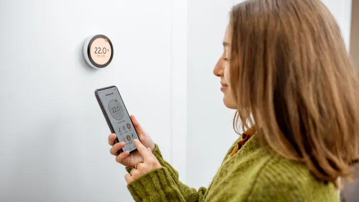 Žena regulující teplotu vytápění telefonem a termostatem doma