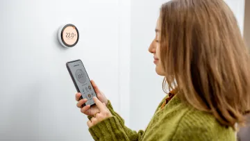 Žena regulující teplotu vytápění telefonem a termostatem doma